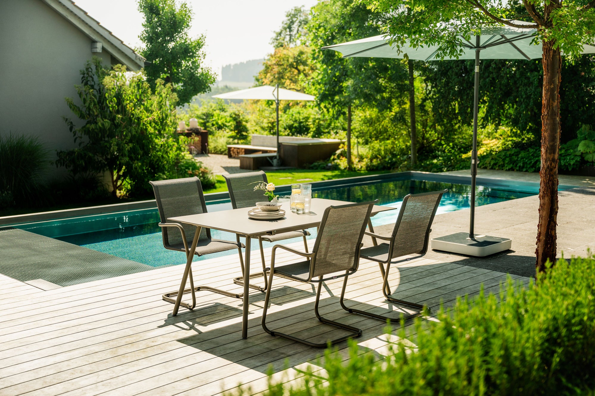 Moderner Gartentisch mit Stühlen auf Terrasse neben Pool und grünem Garten