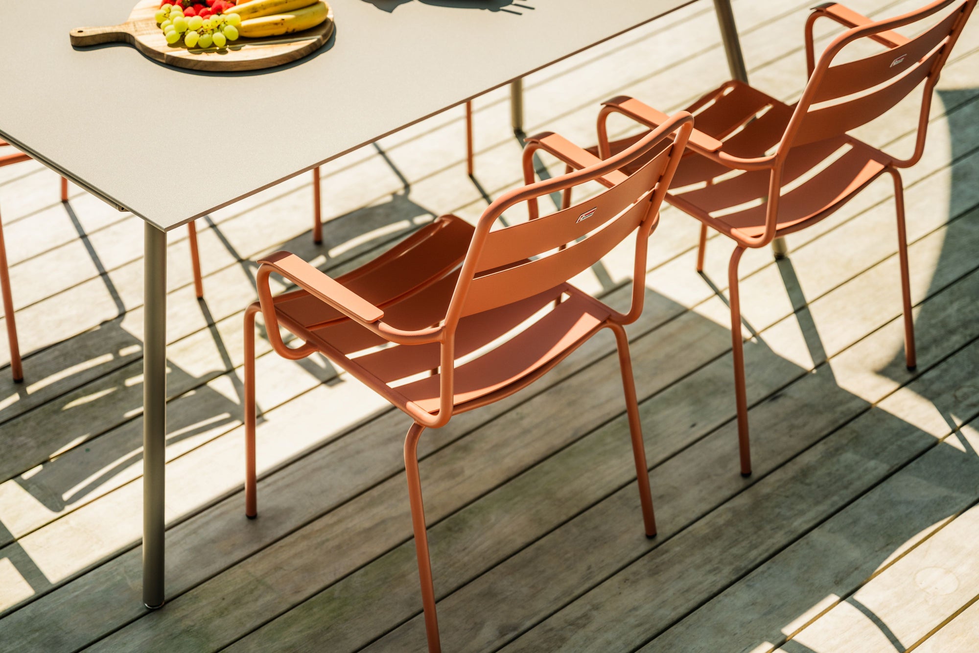 Moderne orange Stühle an Esstisch auf sonniger Terrasse mit Metallgeländer und Holzboden.