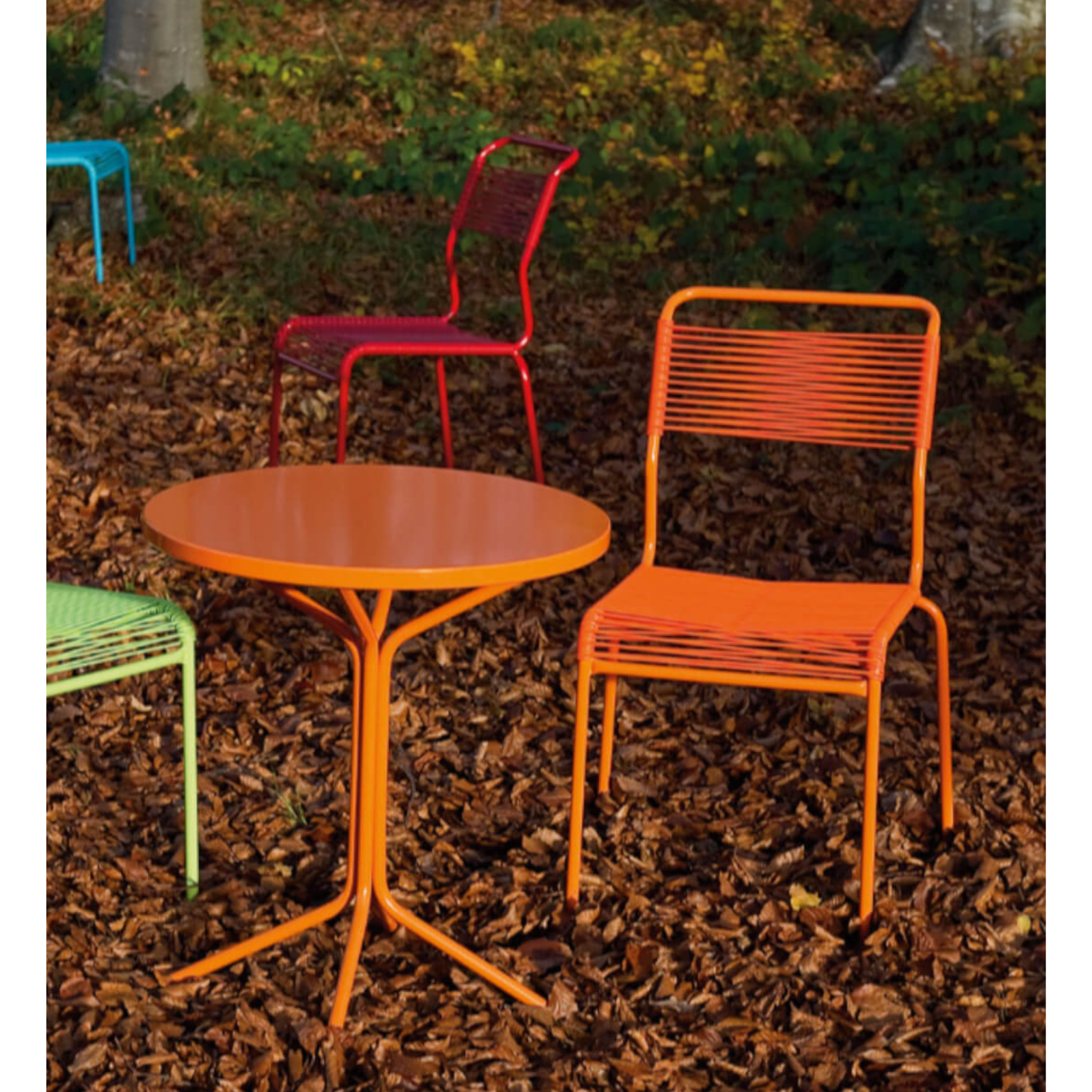 Farbige Gartenmöbel-Garnitur mit orangem Tisch und roten Stühlen auf Rindenmulch