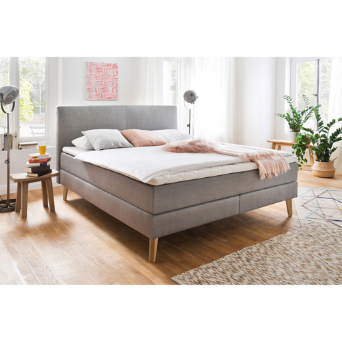 Boxspringbett Greta Porto in Taupe mit Holzbeinen, weisser Bettwäsche und rosa Kissen im hellen Schlafzimmer