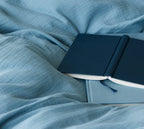 Musselin Bettwäsche Smooth in Blau mit Notizbuch auf Bettlaken, Detail Nahaufnahme